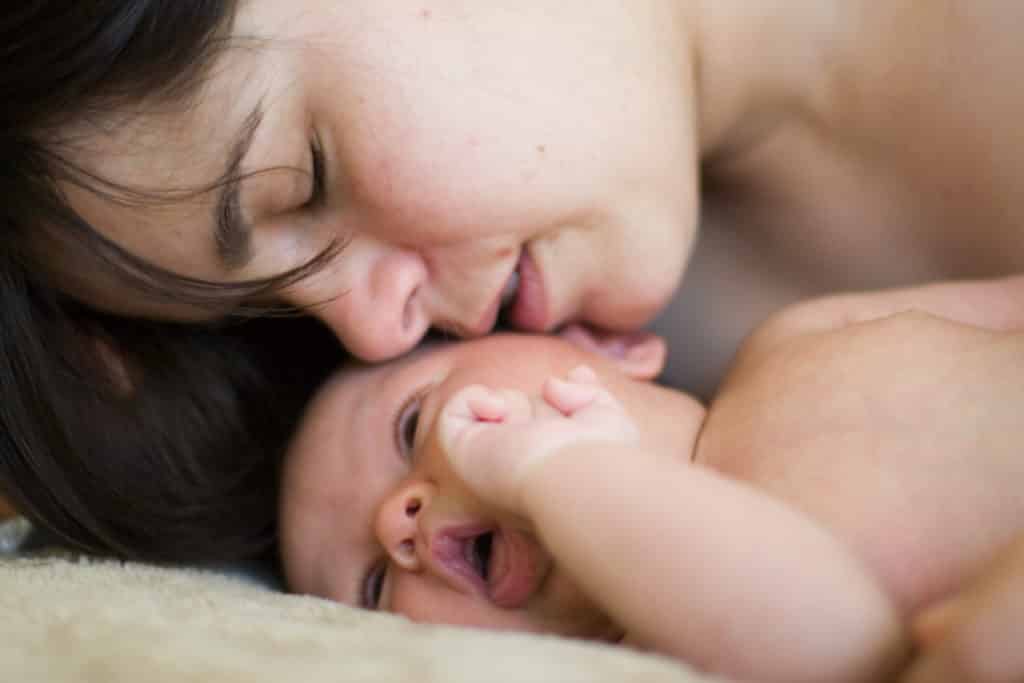 A mother nuzzling and kissing her laughing newborn