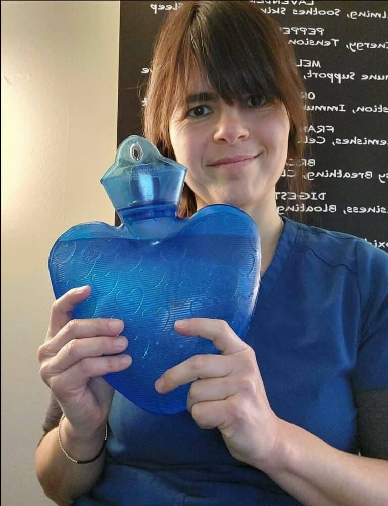 Briana holding a heart-shaped blue hot water bottle in her treatment room